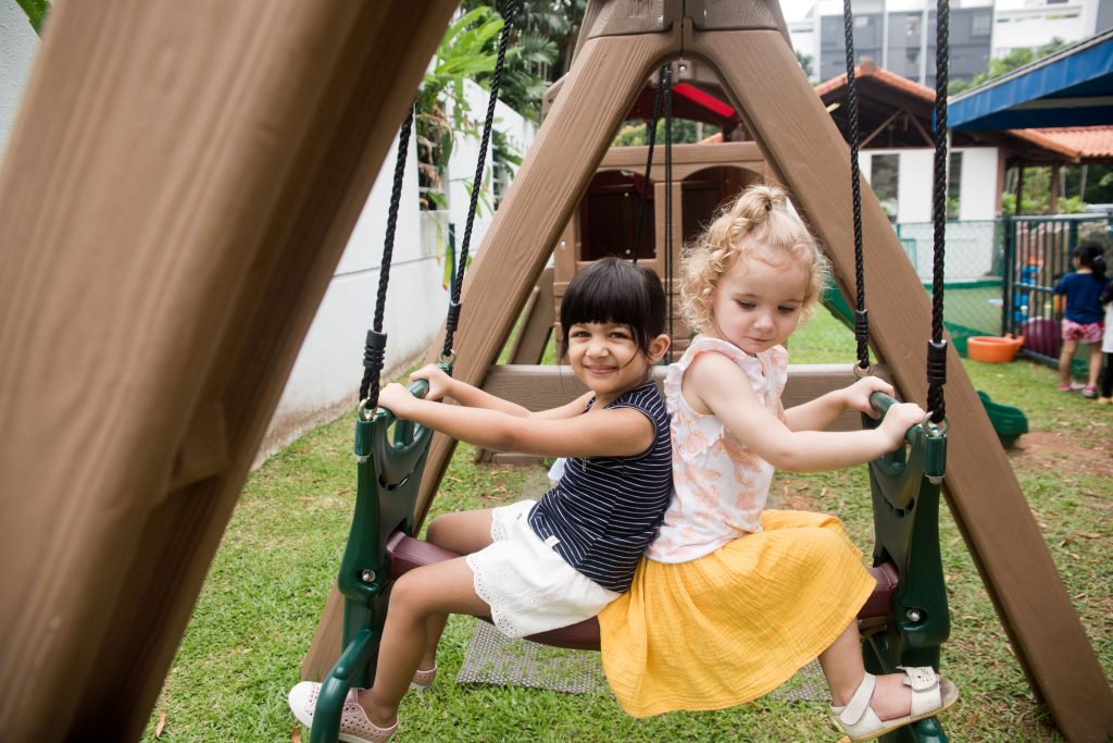 Two girls back to back on a swing