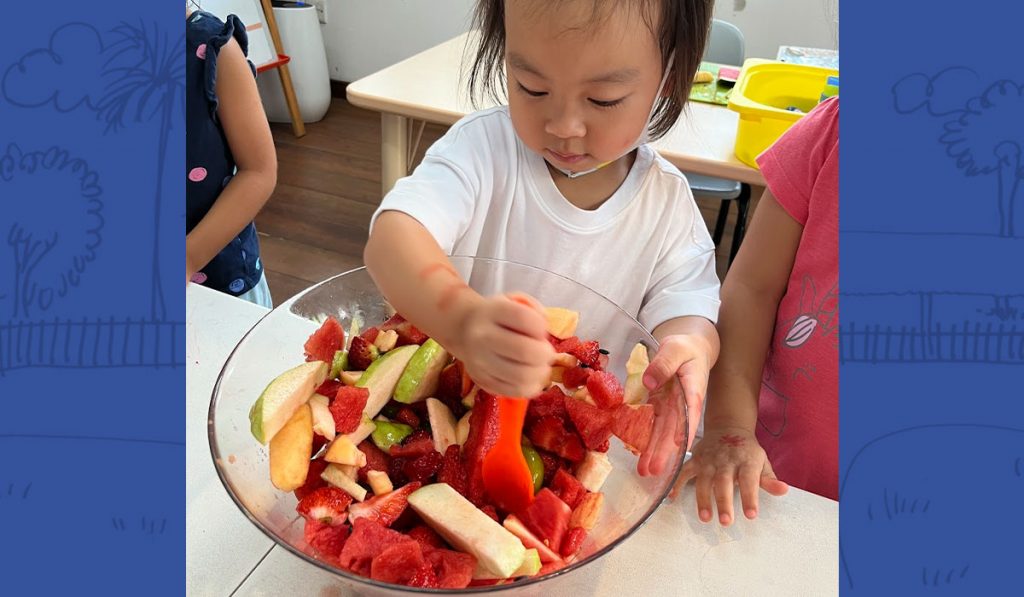 preschooler stirring a bowl of fruits